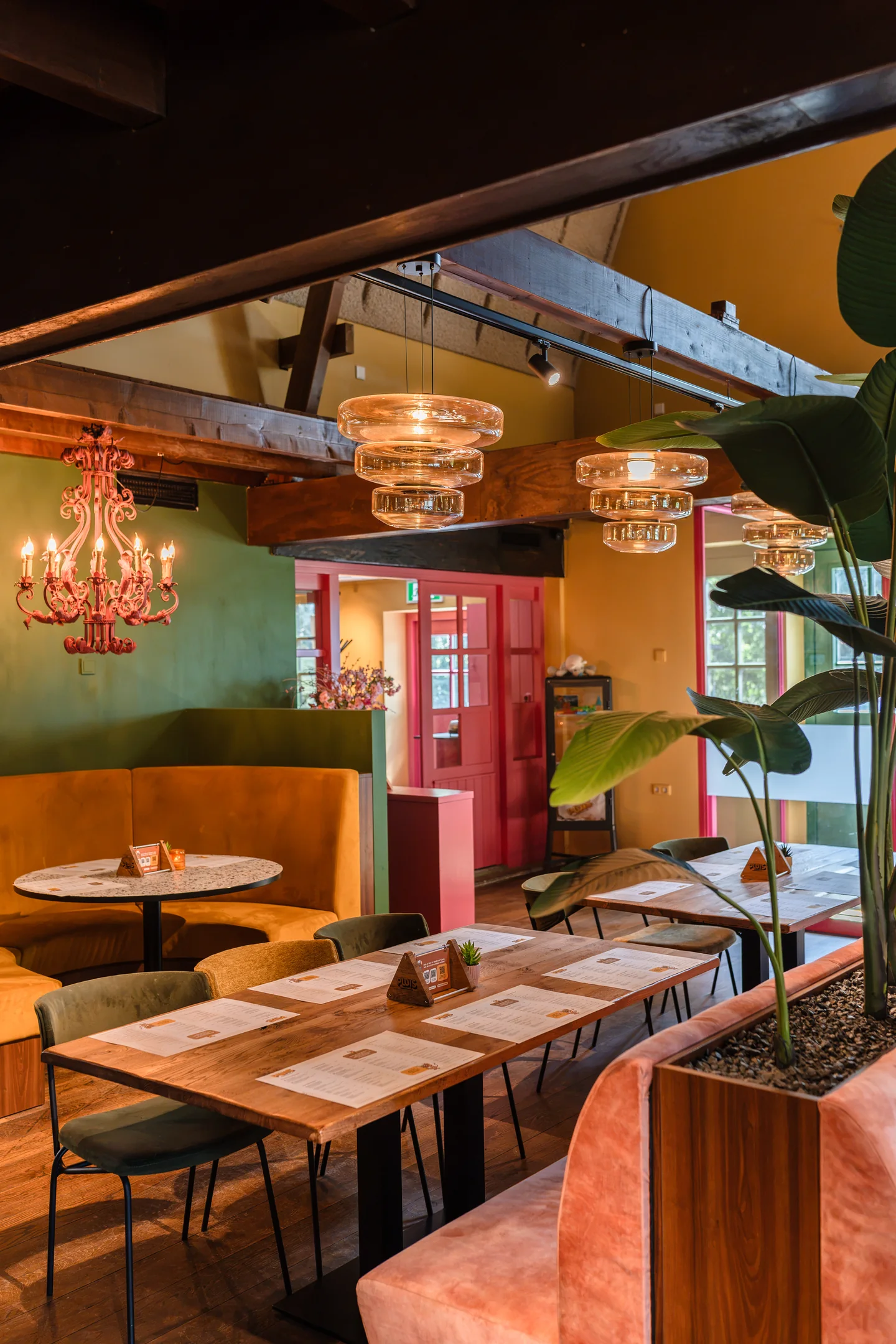 Kleurrijke eetzaal met roze deur en glazen hanglampen bij Familierestaurant Pluis