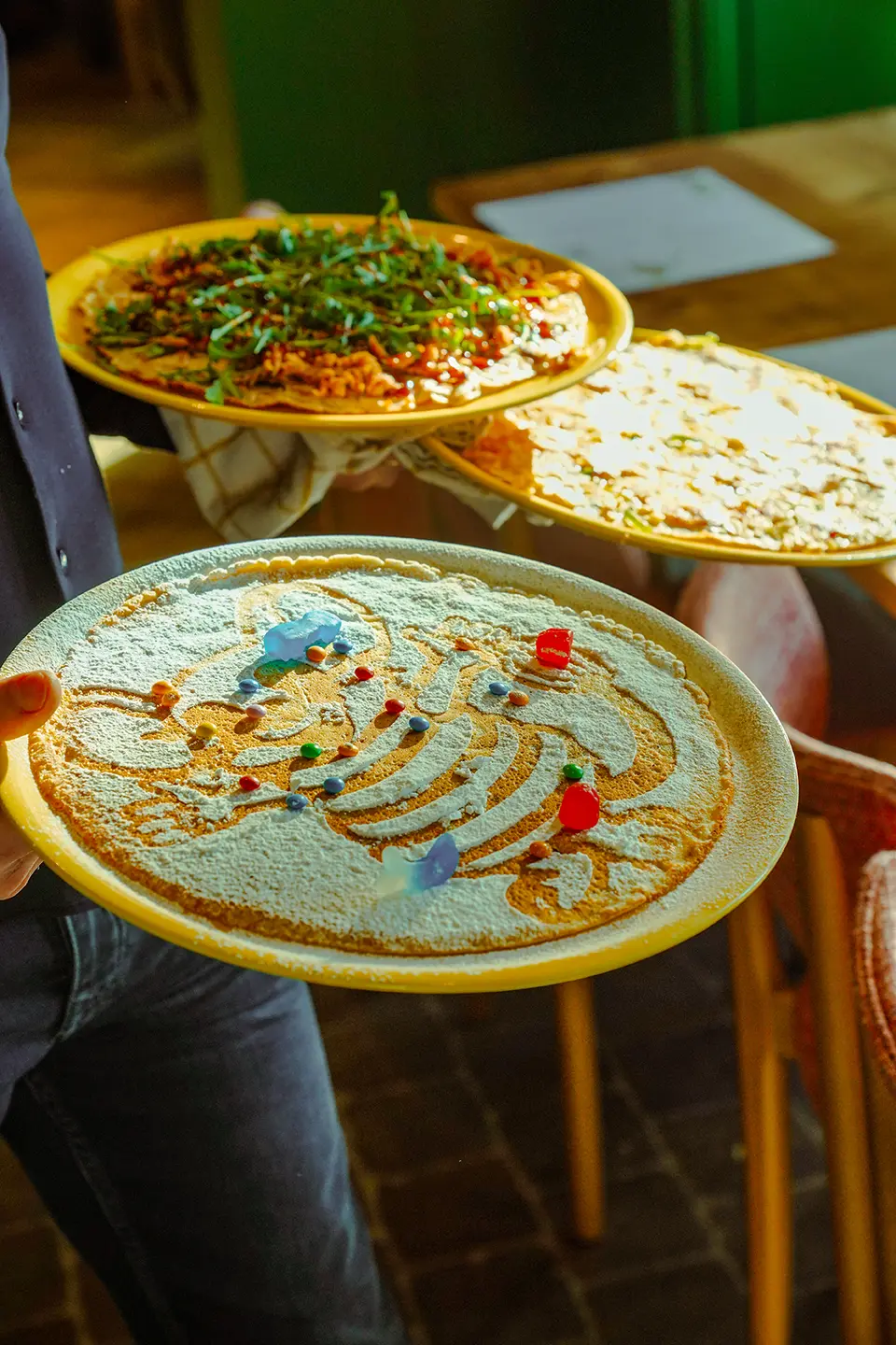 Drie borden met pannenkoeken die naar de tafel worden gebracht, met Pluis in poedersuiker