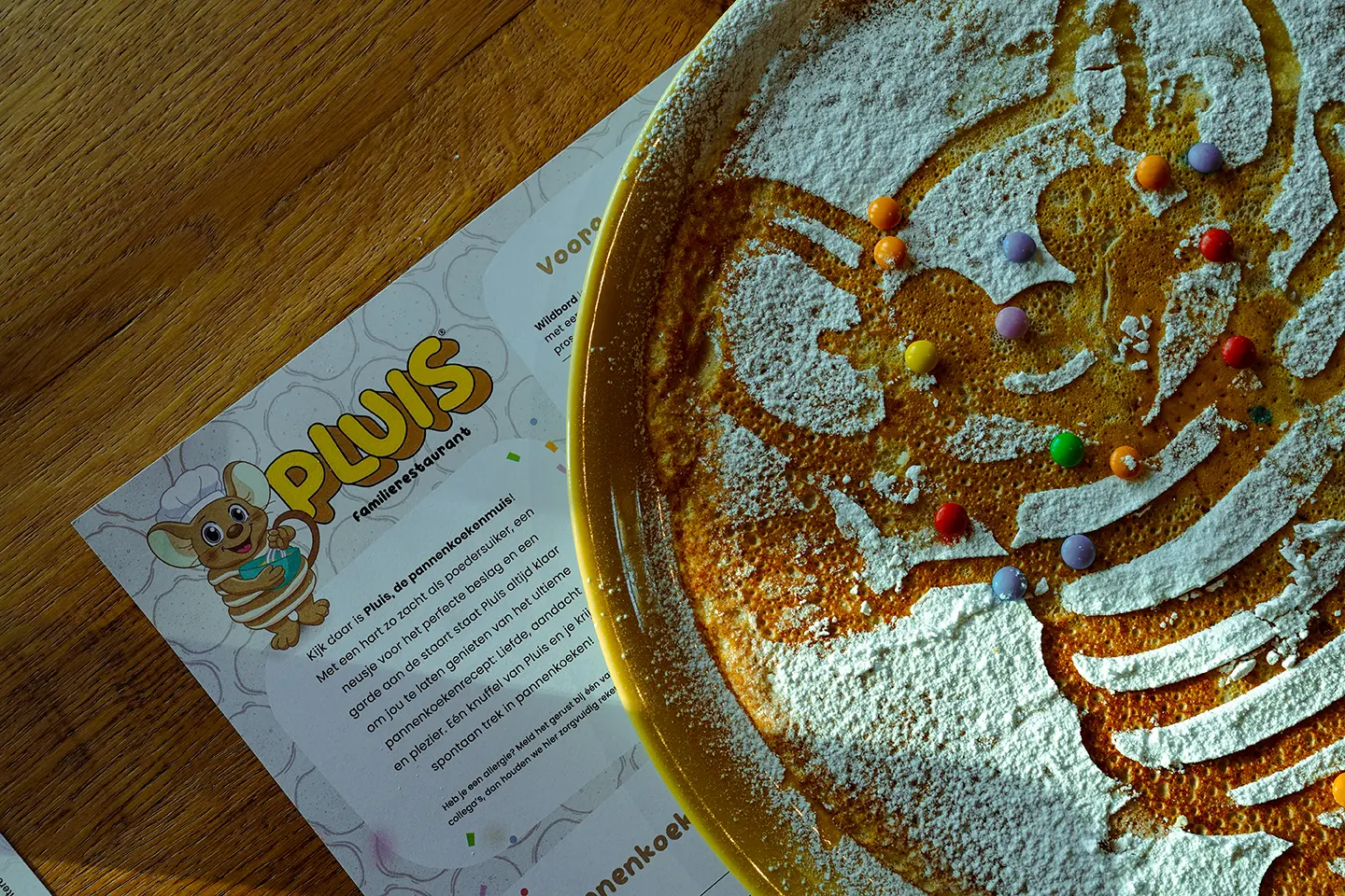 Pannenkoek met poedersuiker in de vorm van Pluis, versierd met gekleurde snoepjes