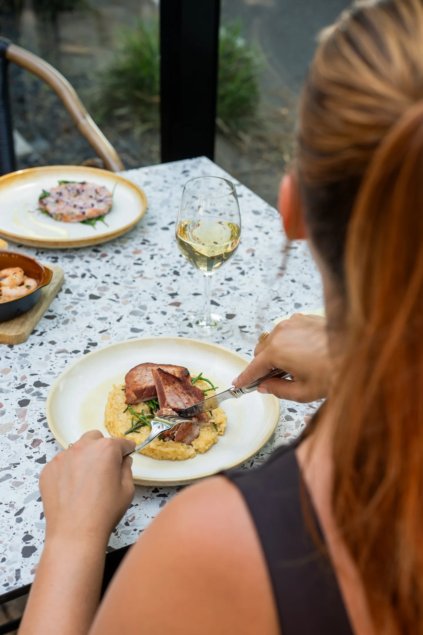 Gast eet hoofdgerecht met glas witte wijn op het terras van Pluis