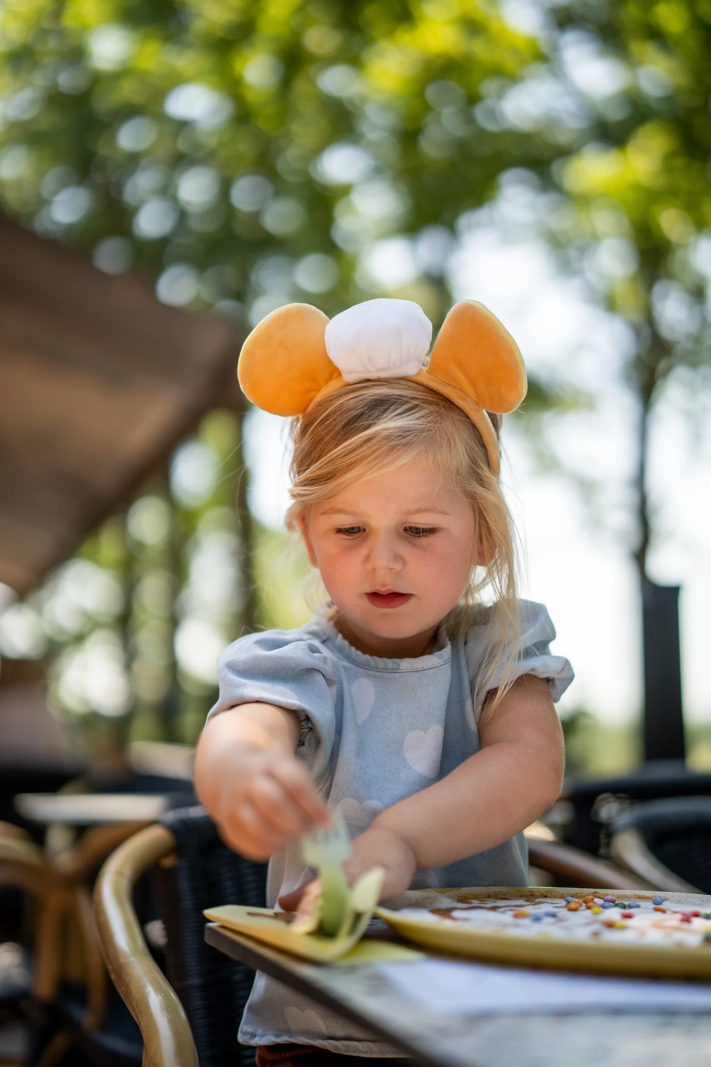 Kind snijdt zelf haar pannenkoek met snoepjes op het zonnige terras van Pluis