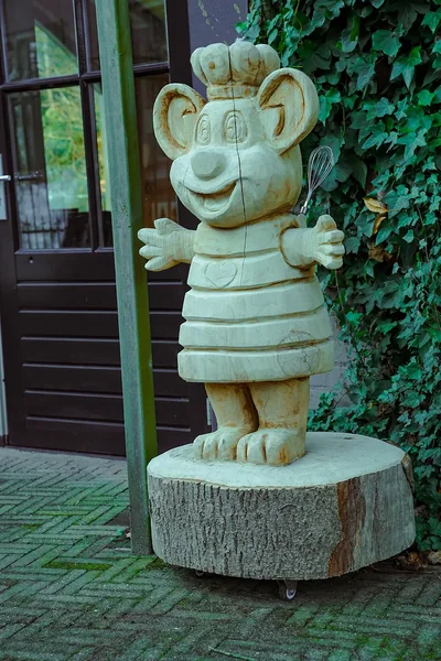 Houten beeld van Pluis de pannenkoekenmuis bij de ingang, naast een muur met klimop