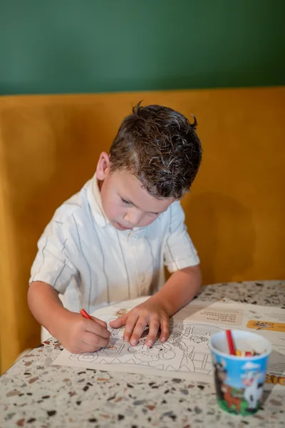 Kind kleurt de kleurplaat van Pluis aan tafel met potloden in de beker