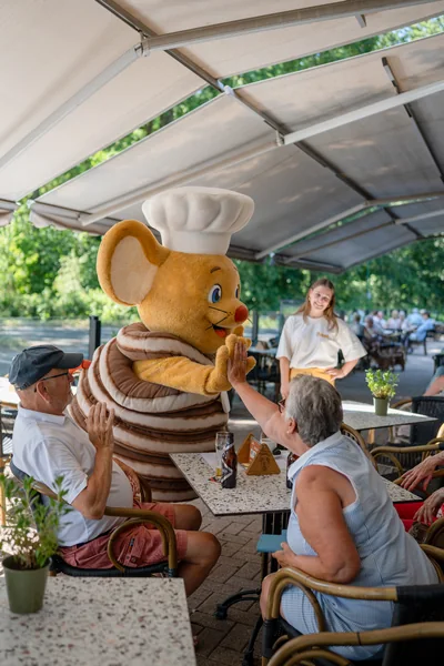 Mascotte Pluis de Pannenkoekenmuis geeft een high five aan gasten op het terras