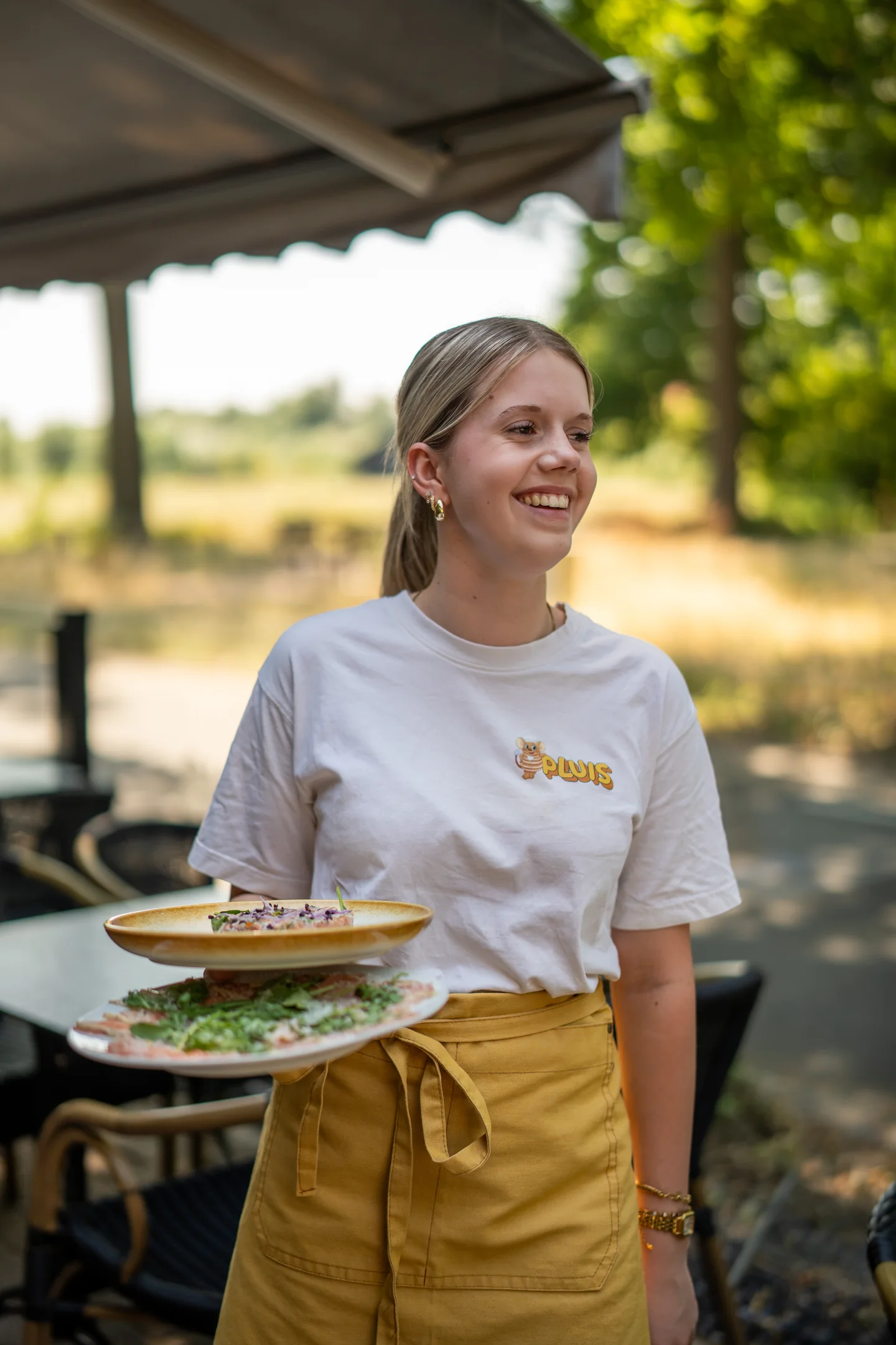 Medewerker van Pluis serveert gerechten op het zonnige terras in Aarle-Rixtel