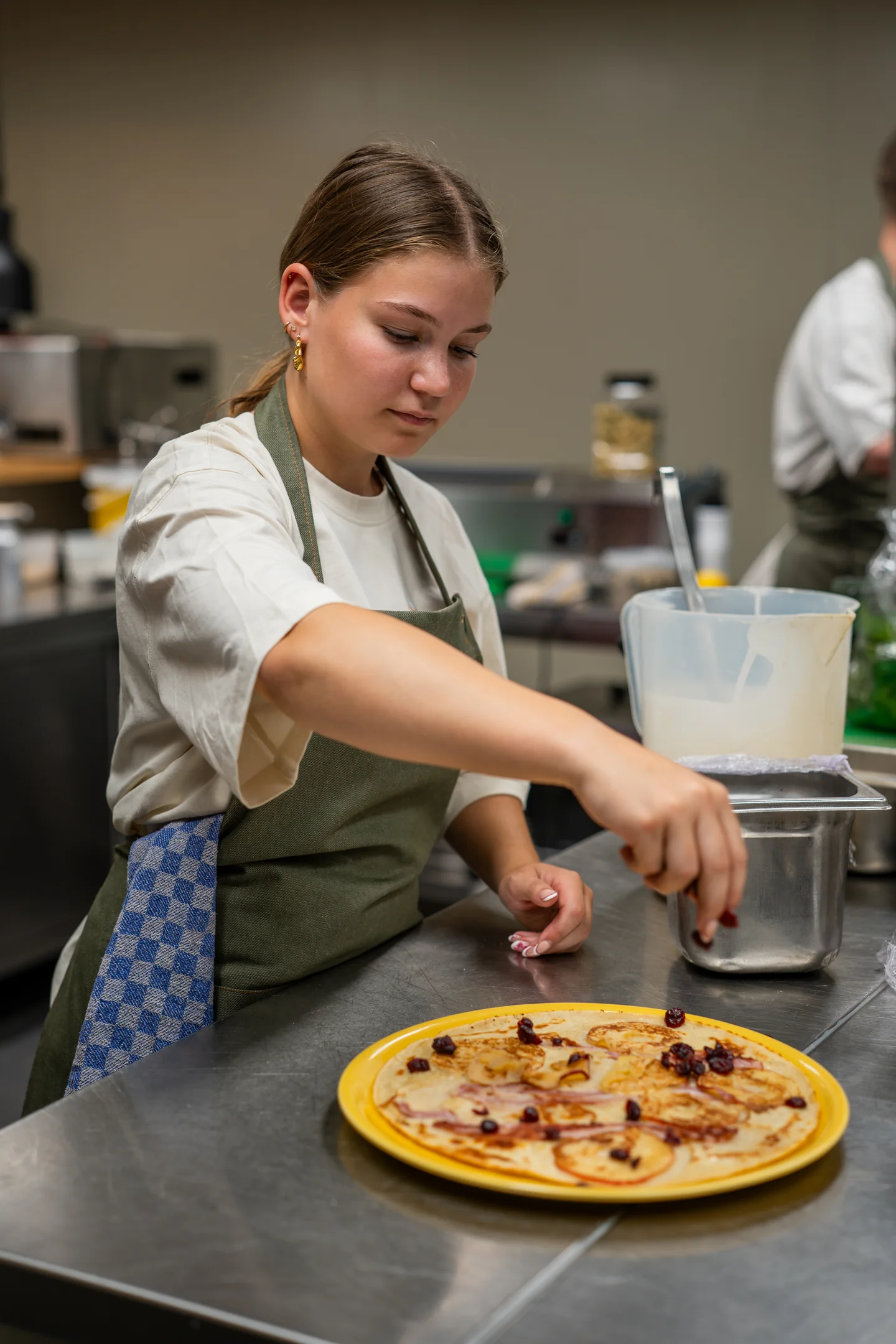 Medewerkster maakt pannenkoek met appel en spek af in de keuken van Pluis