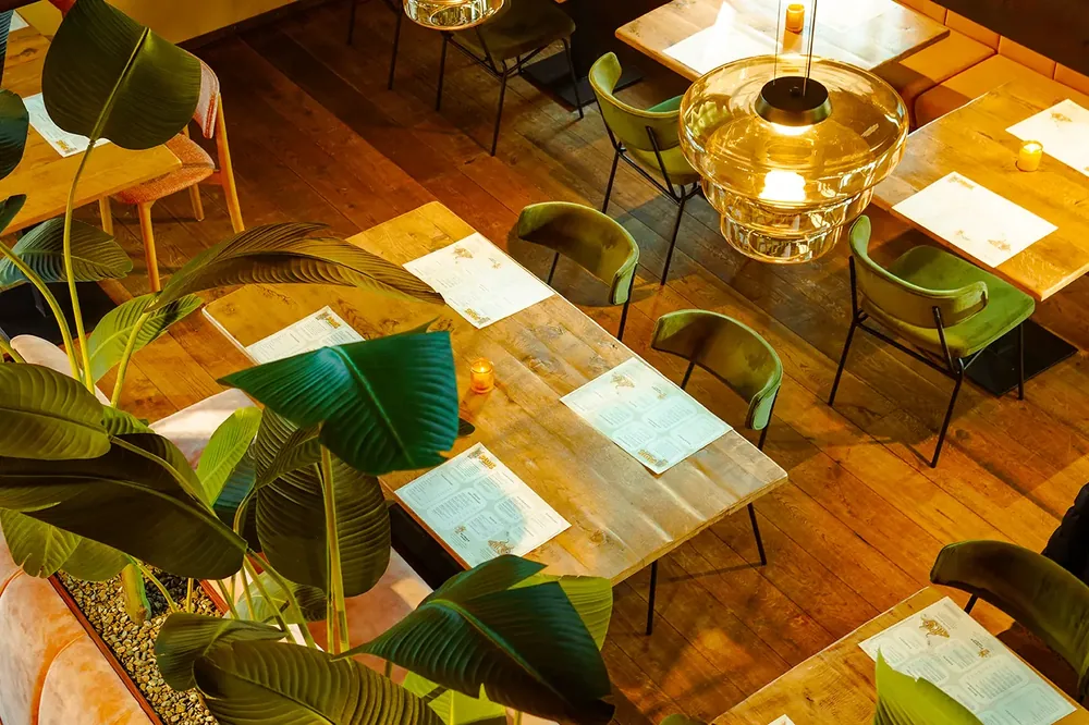 Bovenaanzicht van houten tafels met placemats, planten en gouden hanglampen